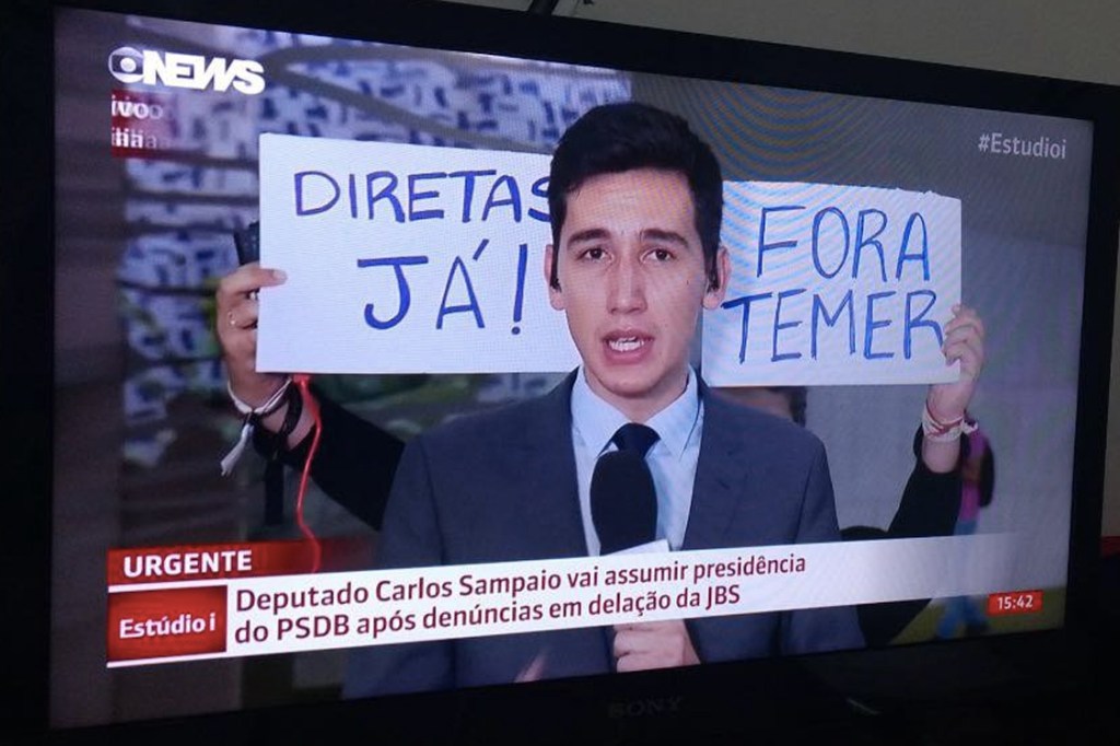 Manifestante segura cartaz em reportagem da Globo News