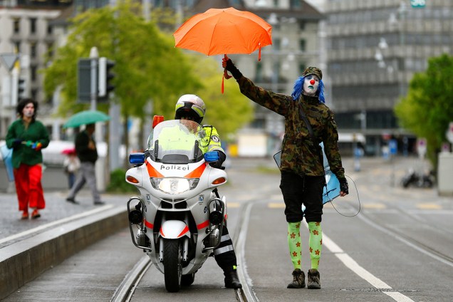 Manifestante vestido de palhaço segura um guarda-chuva sobre um policial, durante protesto do Dia do Trabalho em Zurique, Suíça