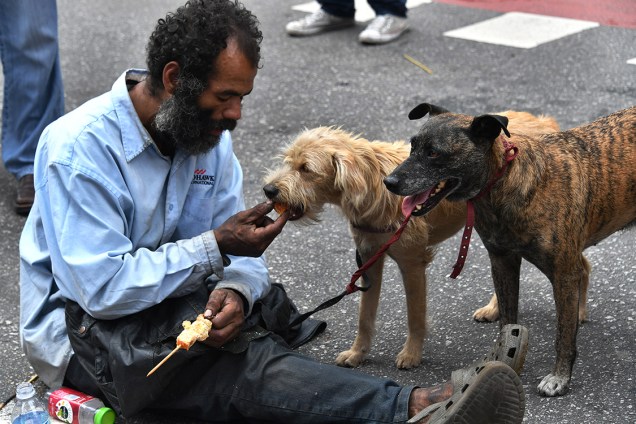 Morador de rua alimenta seus cães na Avenida Paulista, enquanto centrais sindicai fazem ato do Dia do Trabalho, em São Paulo