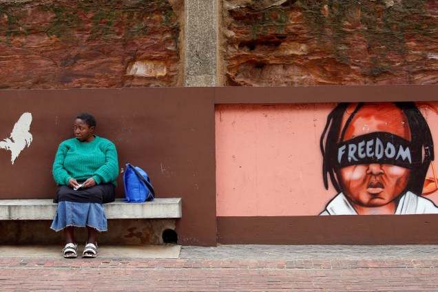 Mulher senta-se ao lado de um mural enquanto membros de partidos de oposição marcham a favor da saída do presidente Jacob Zuma do lado de fora do Tribunal Constitucional em Joanesburgo, África do Sul - 15/05/2017