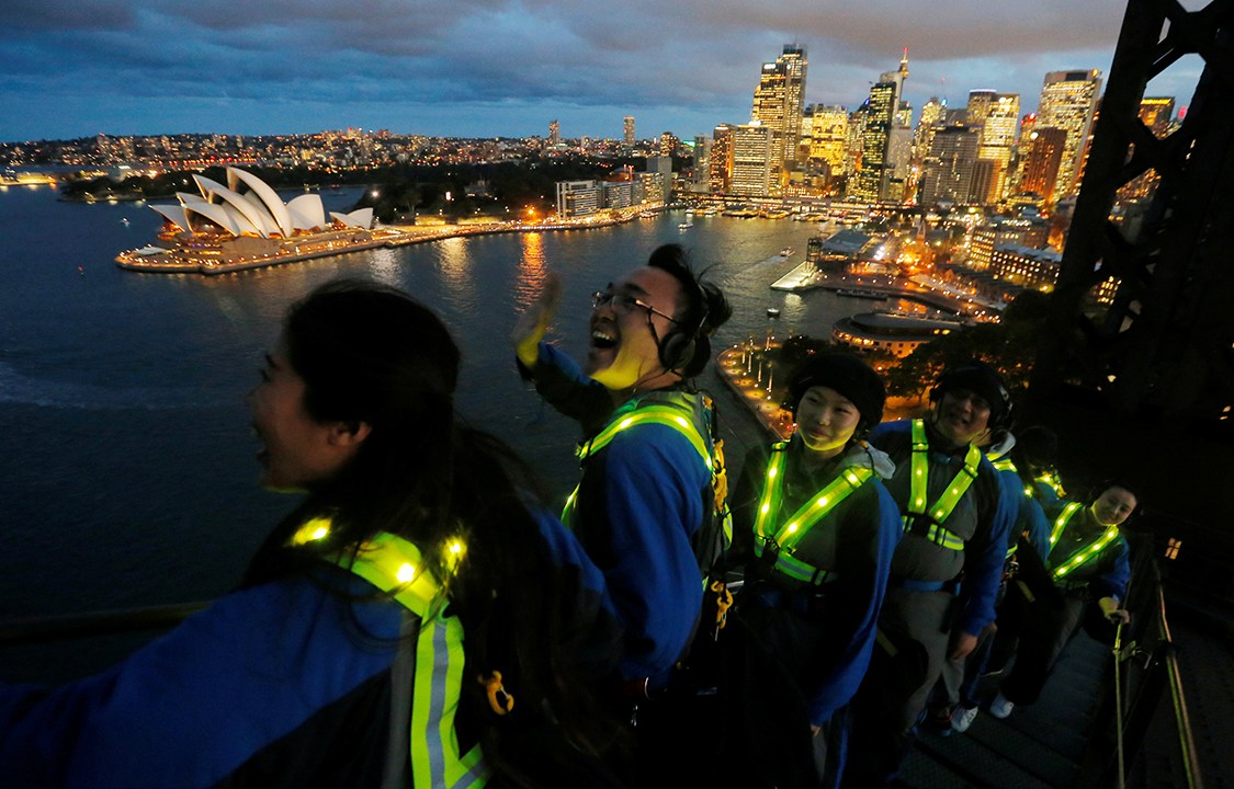 Turitas chineses com roupas fluorescentes visitam o Opera House pela ponte Sydney Harbour, na Austrália