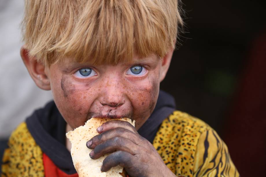 Criança refugiada se alimenta em um acampamento provisório na aldeia de AIn Issa, na Síria