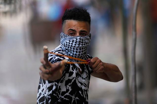 Manifestante palestino usa um estilingue para atirar pedras contra tropas israelenses durante confrontos em um protesto em apoio aos prisioneiros palestinos em greve de fome nas prisões israelenses, na aldeia de Beita, na Cisjordânia - 05/05/2017