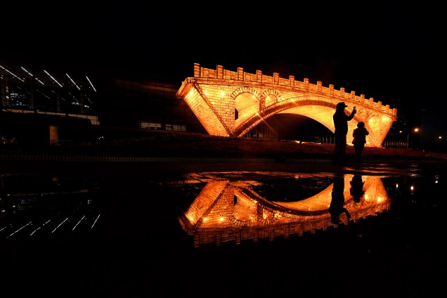 Pessoas tiram fotos em frente à instalação 'Ponte Dourada na Rota da Seda', montada do lado de fora do Centro Nacional de Convenções em Pequim, na China - 11/05/2017
