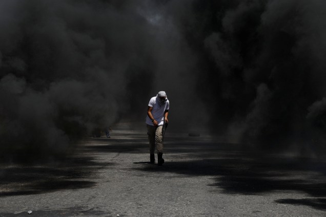 Manifestante palestino fica envolto à fumaça de pneus queimados durante confronto com tropas israelenses em um protesto em apoio a prisioneiros palestinos em greve de fome na cadeias israelenses, perto do assentamento judaico de Beit El, na Cisjordânia - 11/05/2017