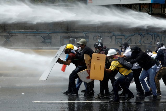 Manifestantes se protegem de jatos de água lançados pela polícia durante protesto contra o presidente Nicolás Maduro - 31/05/2017