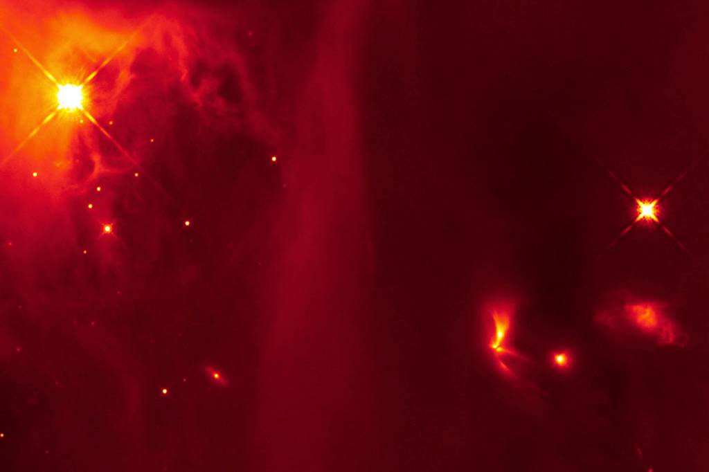Imagem infravermelha do telescópio espacial Hubble contém um objeto brilhante, em forma de ventilador (quadrante inferior direito), que se pensa ser uma estrela binária que emite pulsos de luz à medida que as duas estrelas interagem. O sistema binário primitivo está localizado na nuvem molecular Perseus e foi incluído no estudo pela equipe.