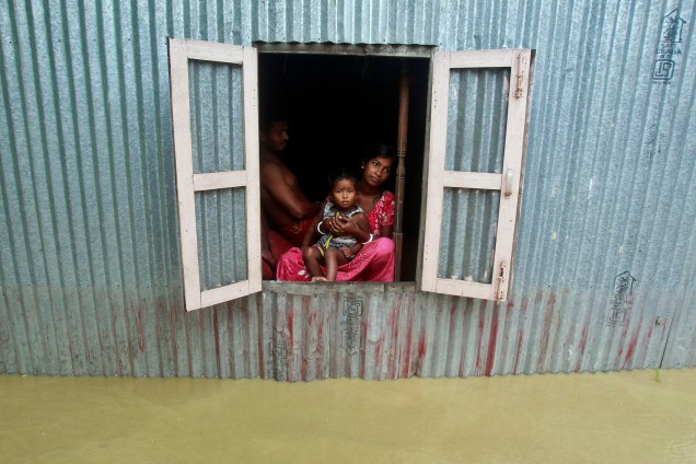 Uma mulher e uma criança olham da janela de casa em uma vila inundada nos arredores de Agartala, na Índia - 19/06/2017