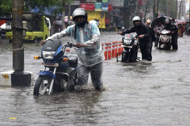 Motoboys empurram suas motocicletas em uma rua inundada durante fortes chuvas em Guwahati, na Índia - 13/06/2017