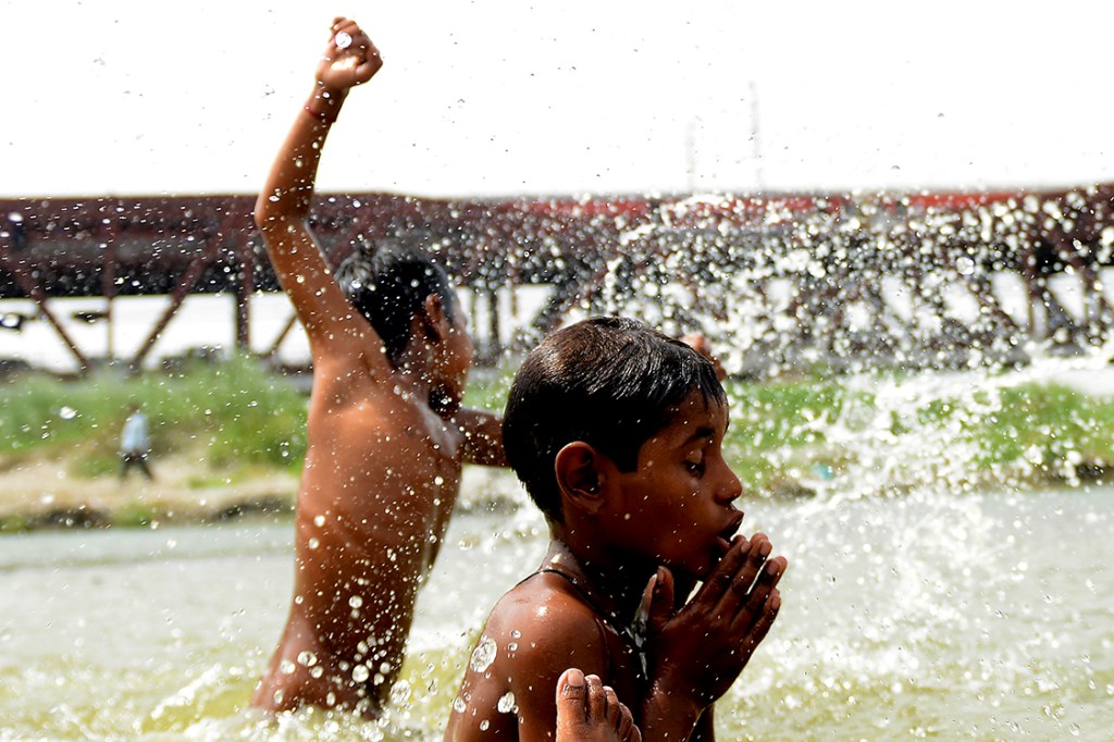 Garotos brincam em um grande lago em Nova Délhi, durante um dia quente com temperaturas registradas acima de 40 graus Celsius, na Índia