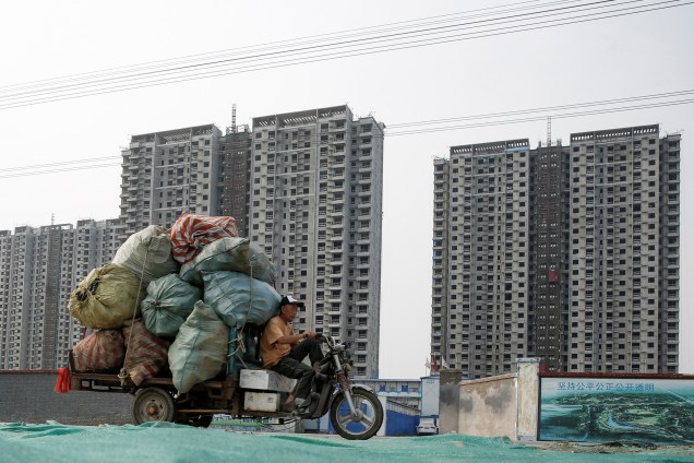 Homem pilota um triciclo carregado com sacos de material de reciclável em frente a um canteiro de obras em Pequim, na China - 27/06/2017