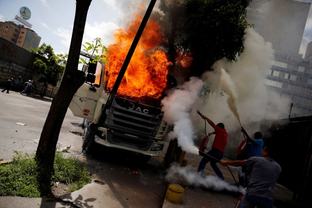 Homens tentam apagar as chamas de um caminhão do governo incendiado durante manifestação contra o governo do presidente Nicolás Maduro em Caracas, na Venezuela - 22/06/2017