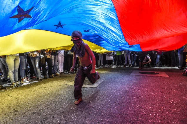 Menino corre sob uma bandeira venezuelana durante protesto de jornalistas e trabalhadores da mídia contra os recentes ataques à imprensa, em Caracas - 27/06/2017