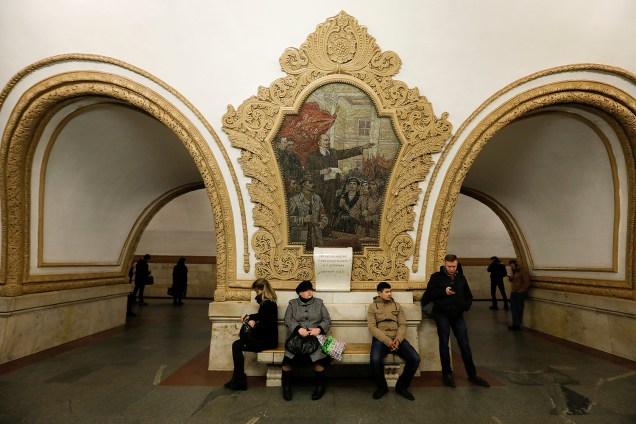 Passageiros esperam o trem em frente a um afresco de Lênin na estação de metrô Kievskaya em Moscou, na Rússia