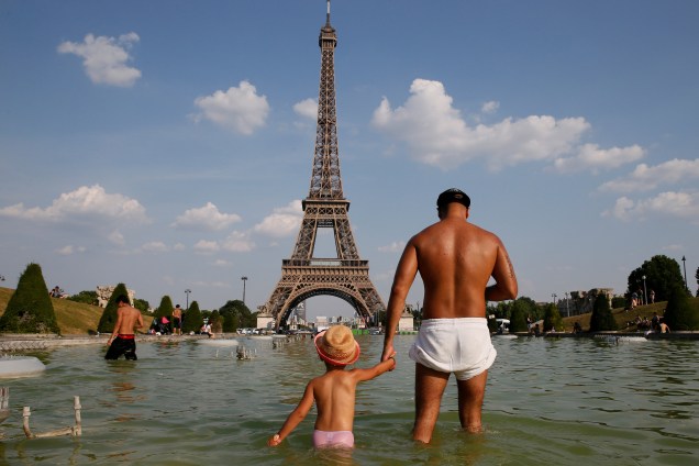 Homem segura a mão de uma criança enquanto se refrescam na fonte Trocadero, perto da torre Eiffel em Paris, na França - 21/06/2017