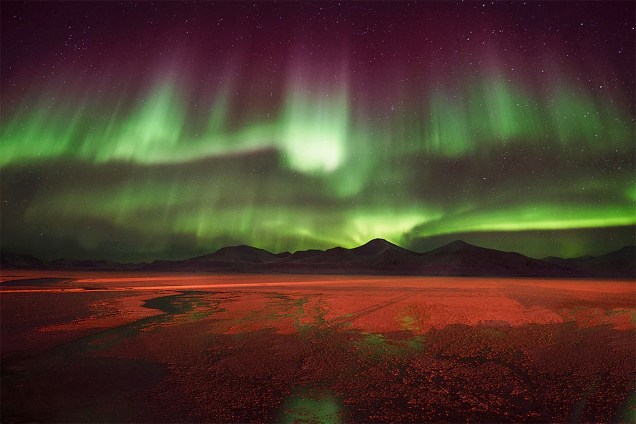 Luzes verdes e roxas de uma aurora boreal iluminando o solo de uma pequena cidade que sobrevive da mineração de carvão, no arquipélago de Svalbard, na Noruega.