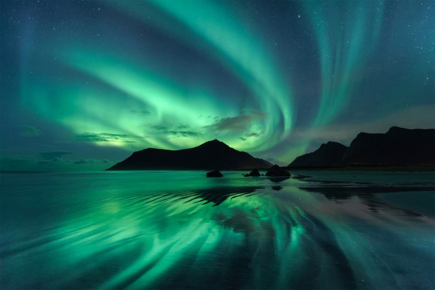 Luzes de uma aurora boreal criam um espelho d'água em <span> Skagsanden, </span>uma praia na Noruega. Para tirar a foto, o fotógrafo teve de esperar o nível da água abaixar.