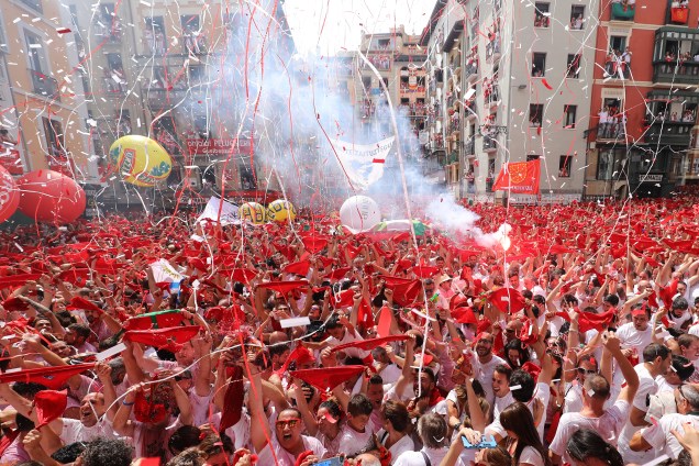 Participantes do Festival de São Firmino seguram bandeirolas vermelhas durante o  'Chupinazo', foguete pirotécnico que indica o início do festival, em frente à Câmara Municipal de Pamplona