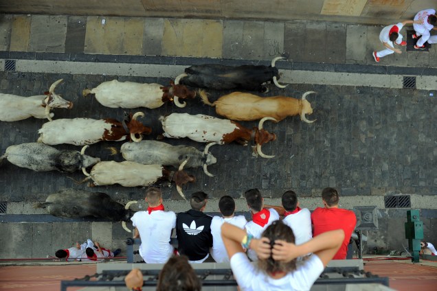 Participantes correm dos touros da raça Cebada Gago durante a tradicional corrida no Festival de São Firmino, em Pamplona, enquanto espectadores acompanham tudo de suas varandas