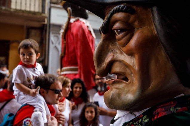 Uma criança olha desconfiada para Caravinagre, um dos personagens que se fantasiam com cabeças gigantes, perseguem e atingem os pequenos durante o desfile no Festival de São Firmino em Pamplona, no norte da Espanha