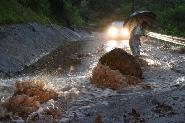 A fotografia da estrada inundada em Hita, na prefeitura de Oita, registra o resultado das fortes chuvas no Japão, rochas foram parar no meio da pista dificultando ainda mais o escoamento da água