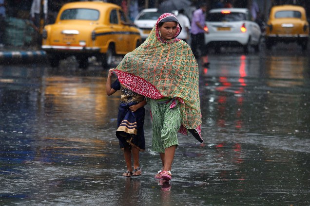 Mulher protege uma criança da chuva enquanto atravessam a rua em Calcutá, na Índia - 06/07/2017
