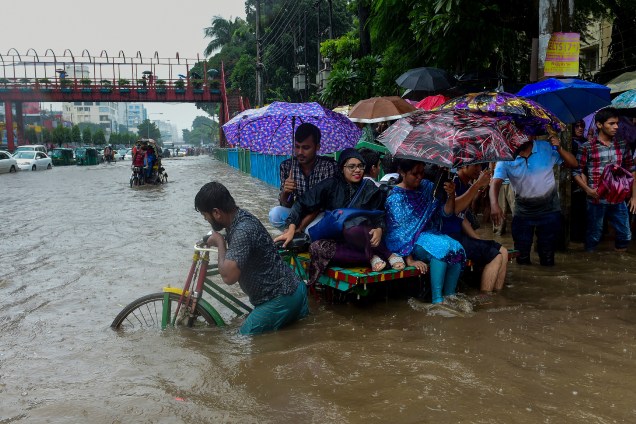 Passageiros usam um riquixá para atravessar uma rua inundada em meio a fortes chuvas em Daca, Bangladesh - 26/07/2017