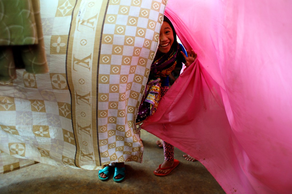 Garota brinca com lençois que separam quartos de famílias em um acampamento improvisado em Marawi, nas Filipinas, após tropas do governo e terroristas entrarem em confronto na cidade