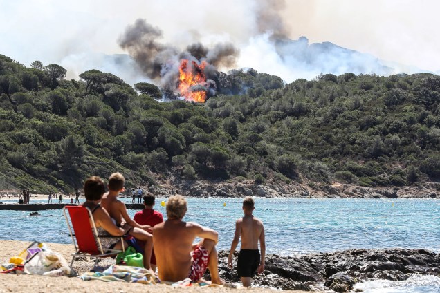 Banhistas desfrutam um dia de sol na praia enquanto olham para um incêndio florestal em La Croix-Valmer, nos arredores de Saint-Tropez, sudeste da França - 25/07/2017
