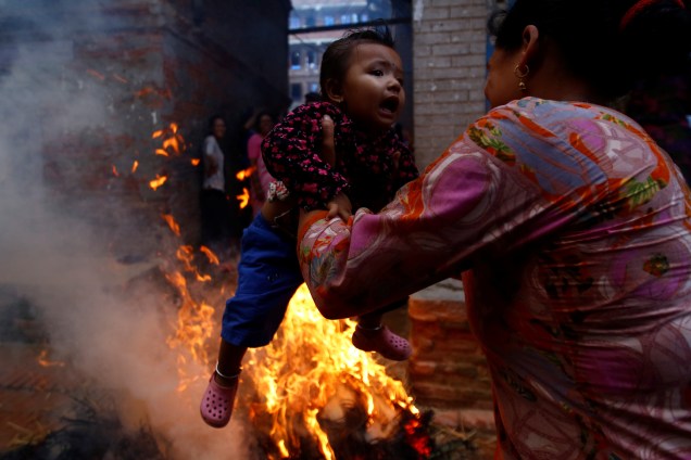 Uma mulher balança uma criança em torno do fogo, onde uma representação do demônio Ghantakarna foi queimada para simbolizar a destruição do mal, durante o festival de Ghantakarna na antiga cidade de Bhaktapur, Nepal - 21/07/2017