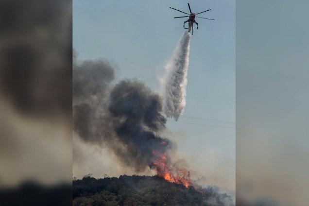 Um helicóptero do corpo de bombeiros despeja água para conter as chamas perto do Forte de Fremont, na estrada 49, depois que as autoridades pediram a evacuação do local devido ao fogo de Detwiler, em Mariposa, Califórnia