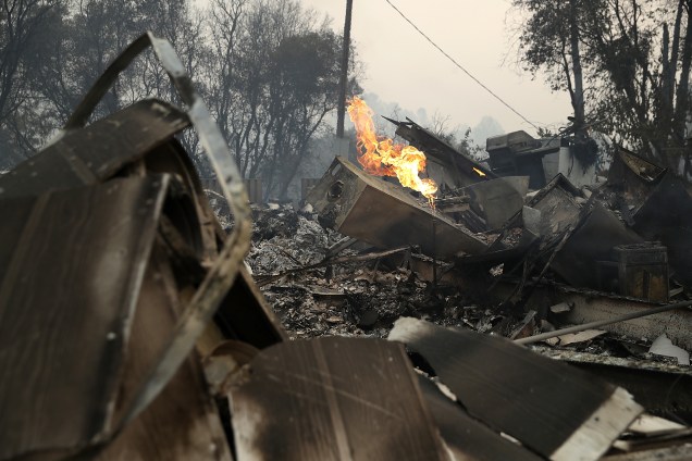 Uma chama de gás em uma casa destruída no incêndio Detwiler continua a queimar na pequena cidade de Mariposa, Califórnia