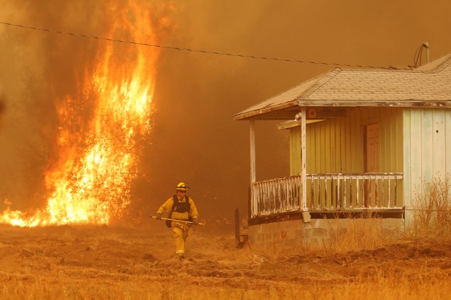 Um bombeiro passa ao lado de uma casa enquanto as chamas do incêndio Detwiler se aproximam rapidamente, na cidade de Mariposa, Califórnia