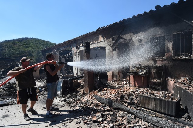 Proprietários de uma empresa de acampamento e caravanismo tentam extinguir as chamas do incêndio em seus edifícios em Bormes-les-Mimosas, na França
