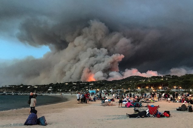 Pessoas que evacuaram suas casas se refugiam na praia e olham para o incêndio que queima a floresta em Bormes-les-Mimosas, no sul da França