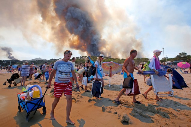 Banhistas deixam a praia em Bormes-les-Mimosas, no departamento de Var, enquanto a fumaça do incêndio florestal toma conta do céu no sudeste da França