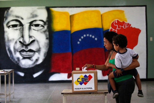 Mulher com uma criança de colo  lança seu voto em frente a um mural do ex-presidente venezuelano Hugo Chávez durante as eleições da Assembleia Constituinte em Caracas, na Venezuela - 30/07/2017