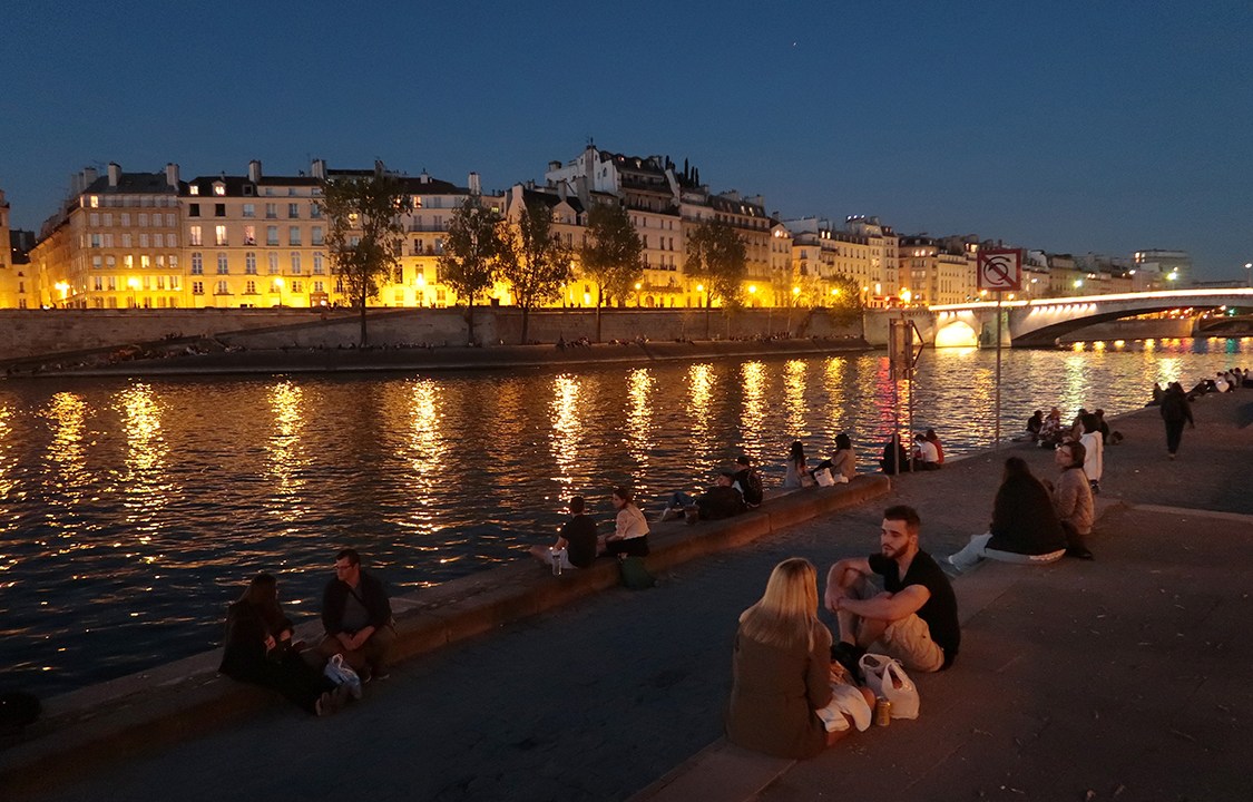 Pessoas conversam e relaxam às margens do Rio Sena, em Paris, França
