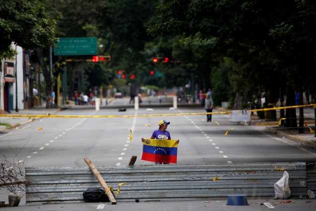Mulher segura bandeira da Venezuela atrás de barricada que bloqueia uma rua em Caracas, durante greve geral convocada pela oposição ao governo de Nicolás Maduro - 26/07/2017