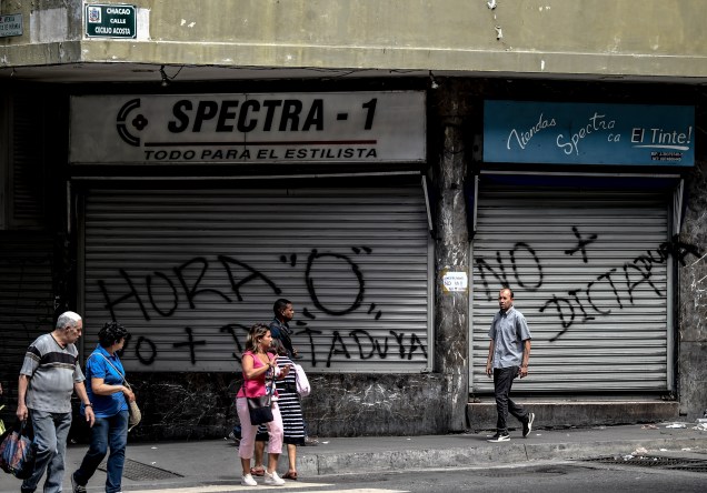 Pessoas passam em frente o comércio que tem suas portas fechadas, devido à greve geral em Caracas contra o presidente venezuelano Nicolás Maduro - 26/07/2017