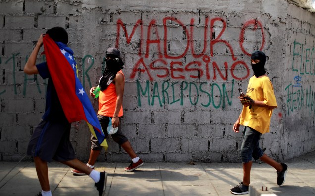 Participantes da oposição venezuelana passam em frente um muro onde está escrito "Maduro Assassino" durante a greve geral contra o presidente, em Caracas - 26/07/2017