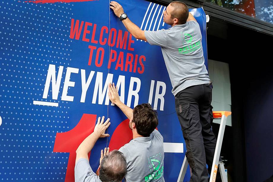 Funcionários de uma loja do PSG na avenida Champs Elysses, em Paris, preparam a fachada com boas-vindas à Neymar
