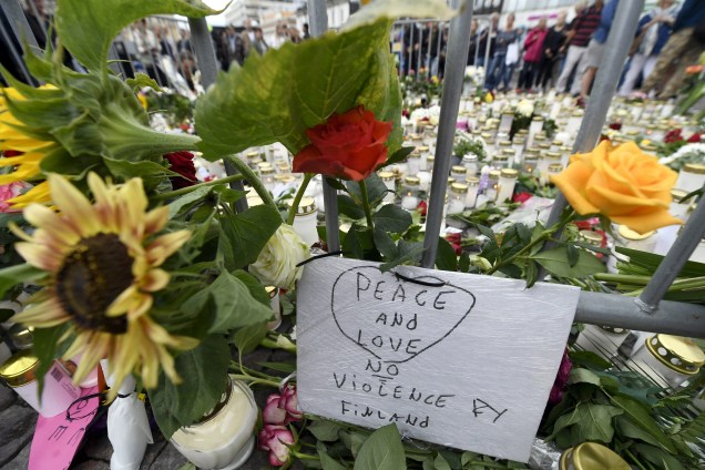 Pessoas levam velas e flores para um memorial improvisado em homenagem às vitimas esfaqueadas na Praça do Mercado, em Turku, na Finlândia