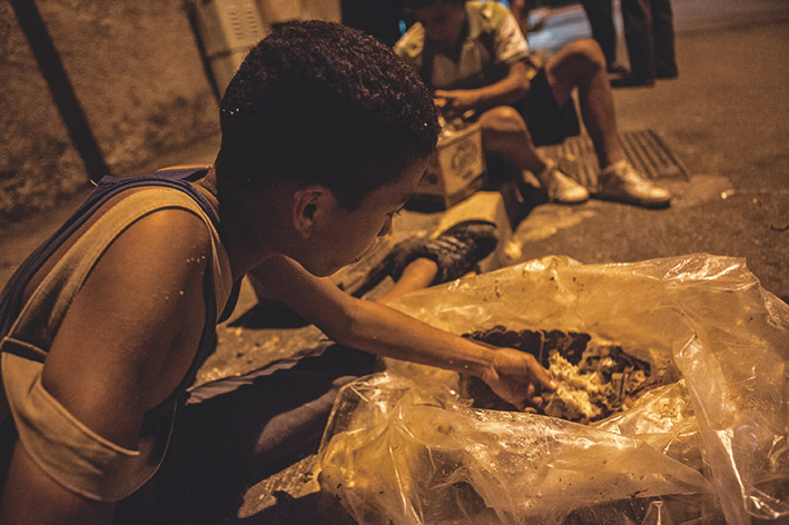 Adolescentes comem jantar retirado do lixo de uma padaria em Caracas, na Venezuela