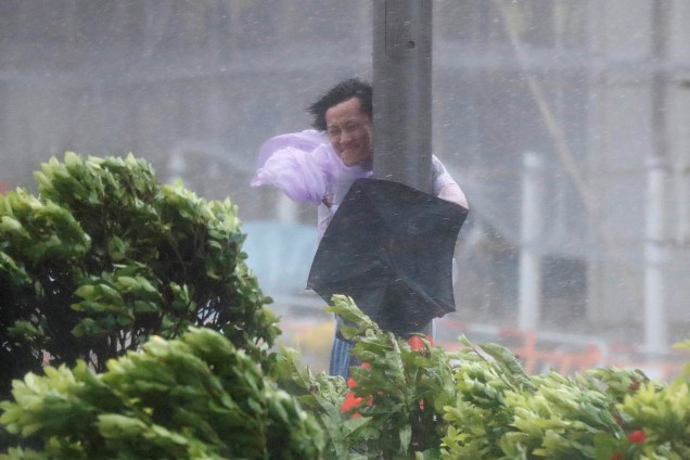 Um homem tenta se segurar em um poste para não voar com os fortes ventos da tempestade causada pelo tufão Hato, em Hong Kong na China - 23/0/2017