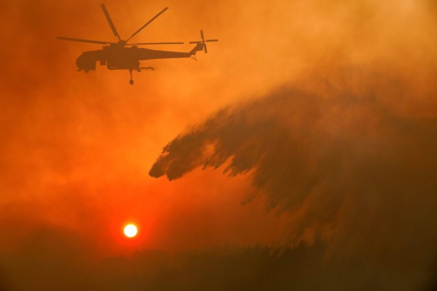 Um helicóptero do corpo de bombeiros despeja água para conter as chamas do incêndio florestal que atingiu a vila de Metochi, no norte de Atenas, Grécia - 15/08/2017