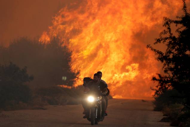 Homens fogem com um cão sobre uma moto de um incêndio florestal perto da vila de Varnavas, ao norte de Atenas, na Grécia - 14/08/2017