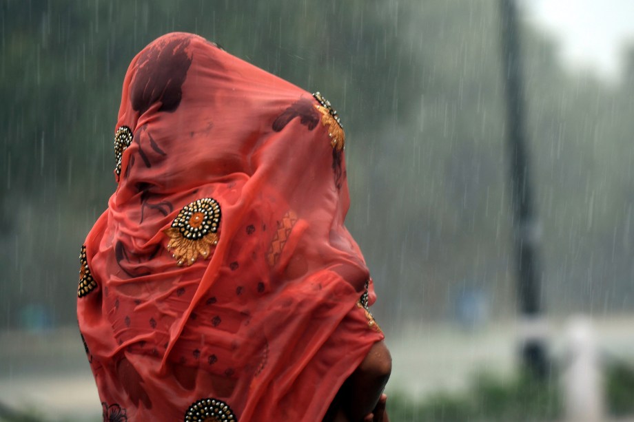 Mulher indiana cobre seu bebê com um pano vermelho durante uma forte chuva em Nova Deli - 07/08/2017