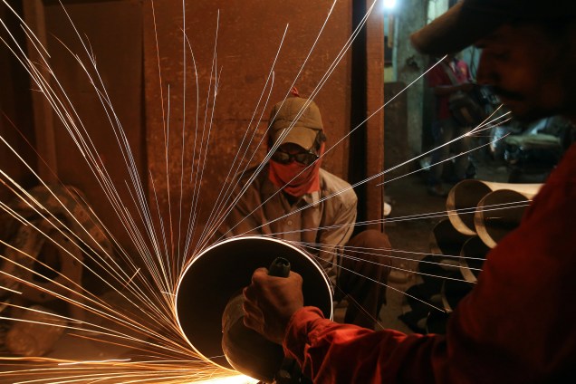 Trabalhadores usam uma serra elétrica para cortar canos em uma fábrica de tubos de metal, em Mumbai, na Índia - 11/08/2017