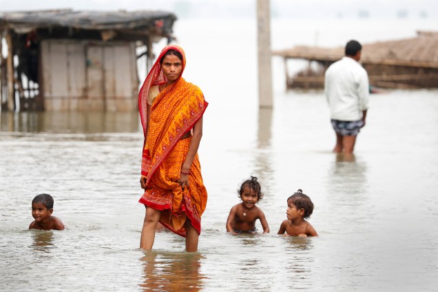Enquanto crianças brincam na água, uma mulher caminha por uma vila inundada na cidade de Motihari, Bihar, na Índia - 23/08/2017